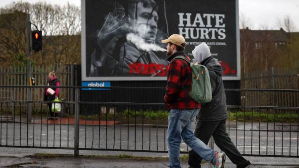 Two men walk in front of an anti-hate billboard in Glasgow, Scotland.