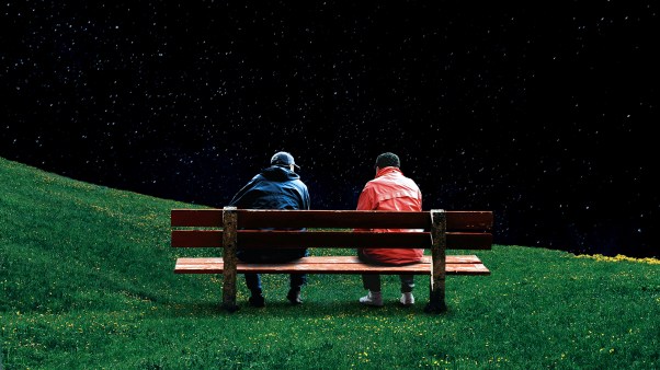 Two people in red and blue jackets sitting on a bench together.