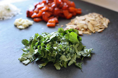 Chopped cilantro, roasted peppers and almonds on a black cutting board.