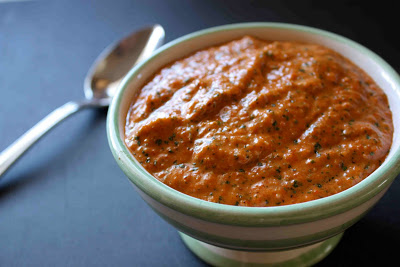 Bowl of red pepper and cilantro pesto on black surface.