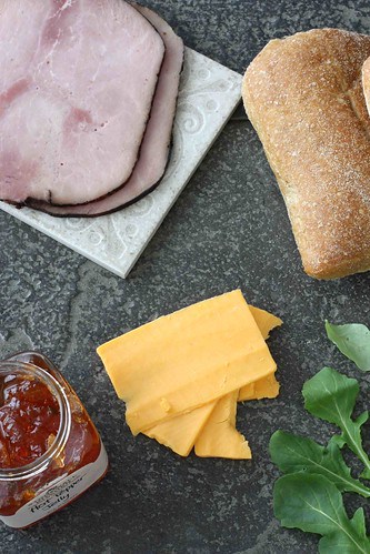 Ciabatta, ham, pepper jelly and cheese slices on a cutting board.