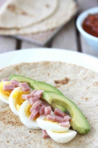 A tortilla topped with hard boiled egg, avocado and ham.