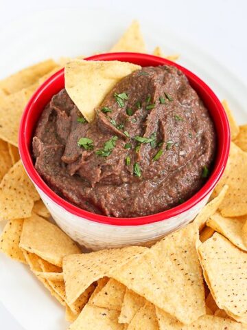 Black bean dip in a red bowl, on a white plate with tortilla chips.