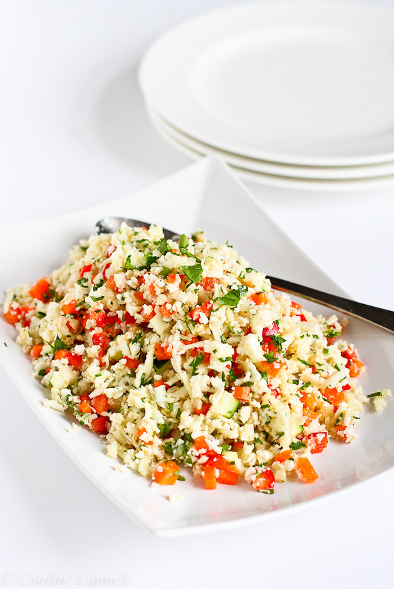 Grated cauliflower salad on a white dish with white plates behind.