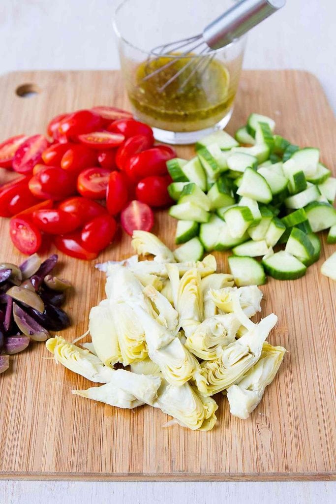 Tomatoes, diced cucumber, artichokes, olives and lemon vinaigrette on a wooden cutting board.