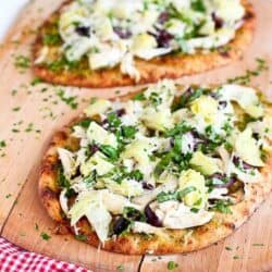 Two naan pizzas on pizza peel, topped with chicken and artichoke hearts.