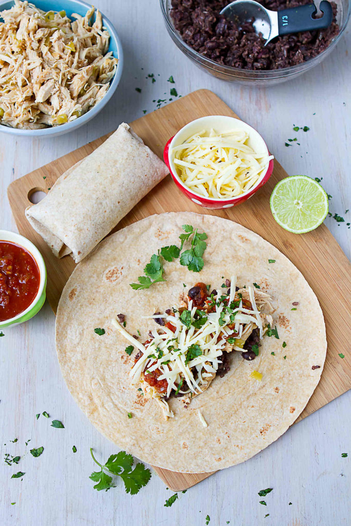 Assembling chicken, black beans and rice burritos on a cutting board.