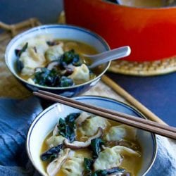 Wonton soup with mushrooms and chard in bowls. Spoons and chopsticks on the side.