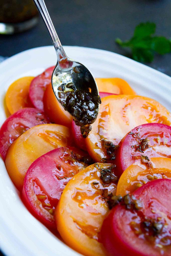 Drizzling a shallot balsamic vinaigrette over sliced tomatoes.