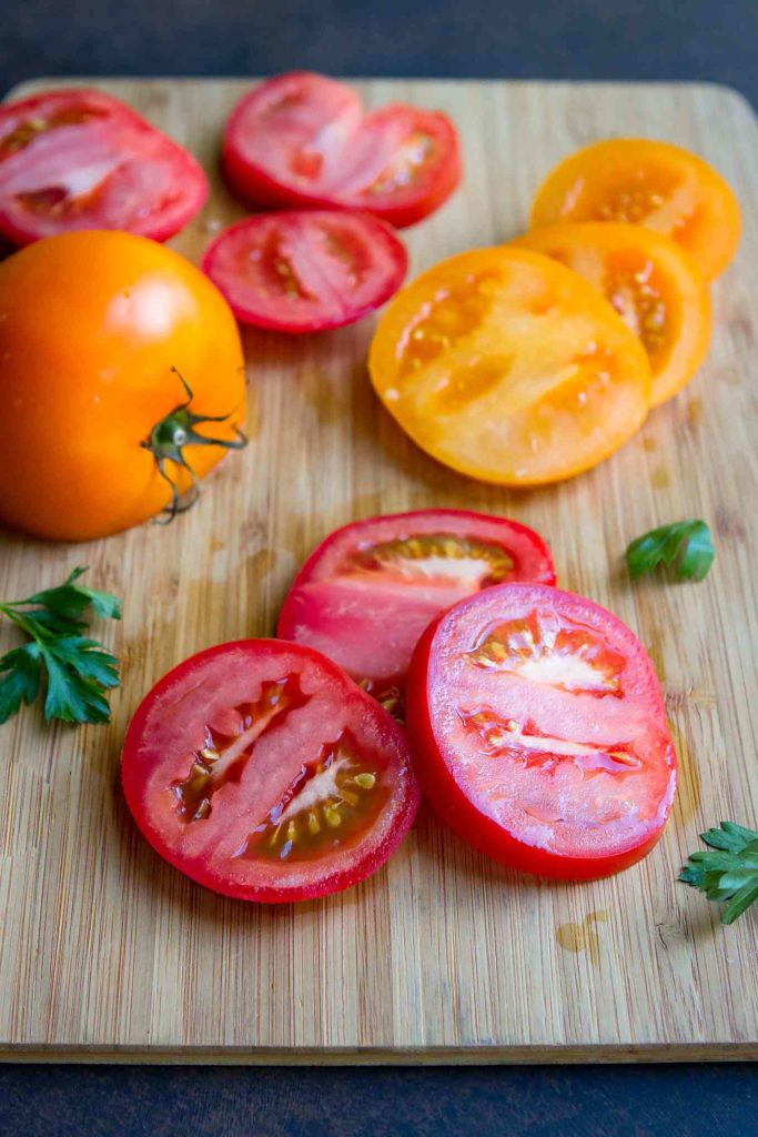 Sliced orange and red heirloom tomatoes on a bamboo cutting board.