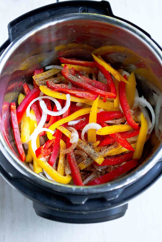 Bell pepper strips and sliced onions in a pressure cooker.