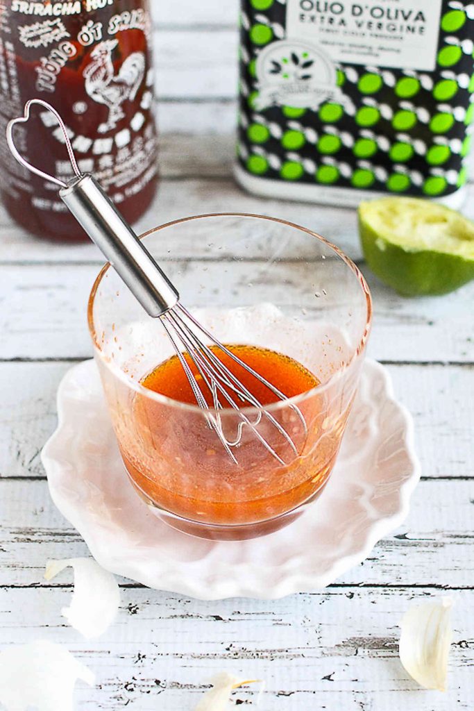 Sriracha lime vinaigrette in a glass with a whisk