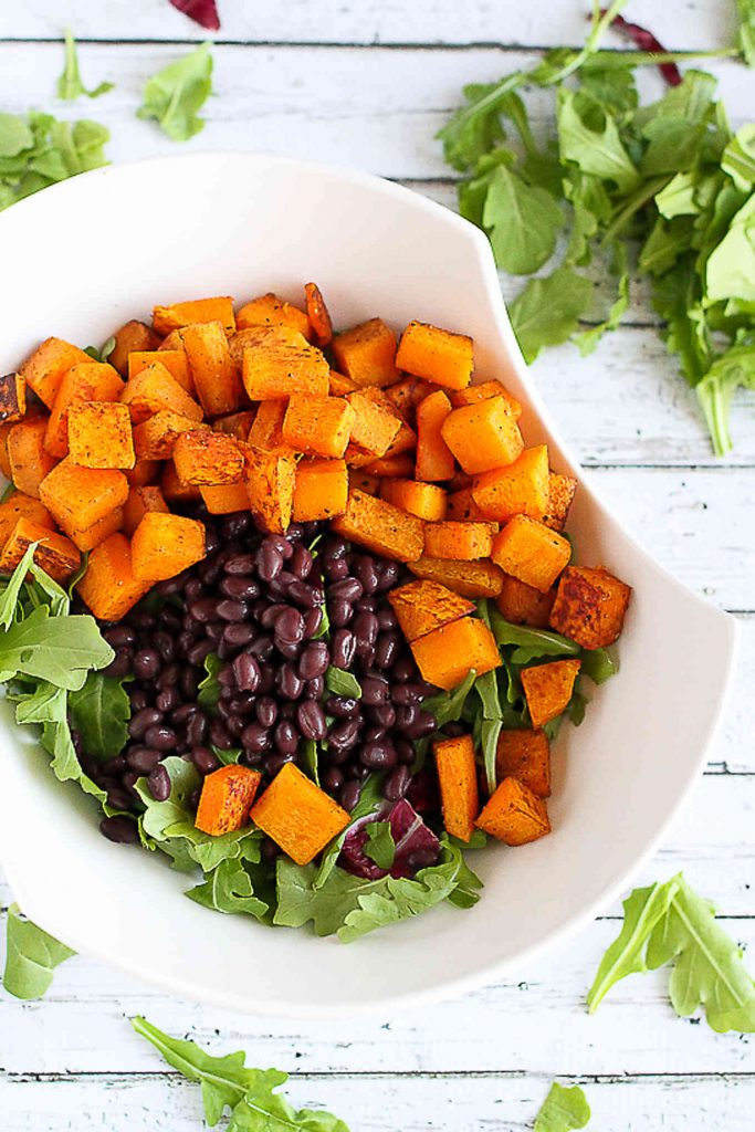 Roasted squash, black beans and arugula in a large white bowl.