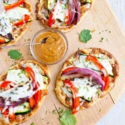 Overhead photo of Thai veggie naan bread pizzas on a pizza peel, with a bowl of peanut sauce.