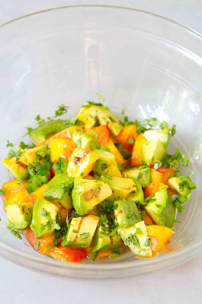 Chunks of grilled avocado, grilled peach and cilantro in a glass bowl.