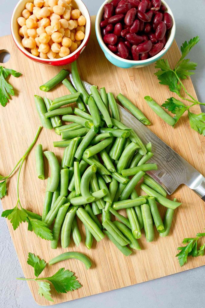 Green beans on a bamboo board, chickpeas and kidney beans in bowls.