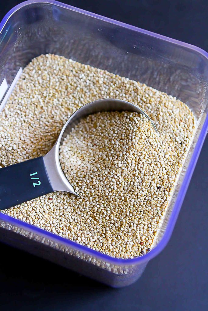 Clear storage container filled with quinoa. Measuring cup dipping into the quinoa.