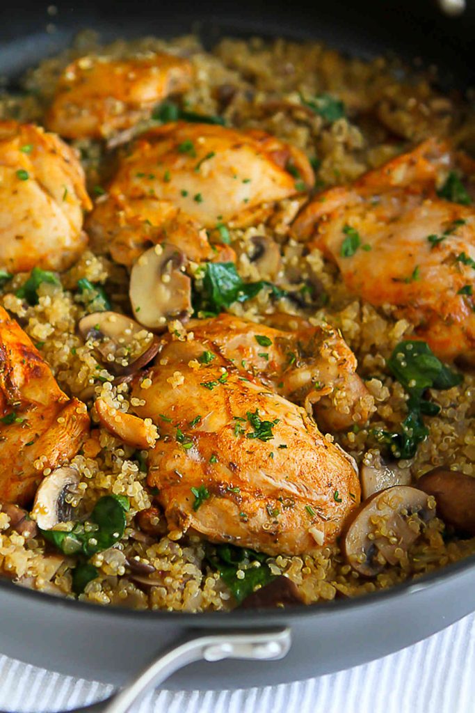 Chicken thighs, cooked quinoa, mushrooms and spinach in a black skillet.