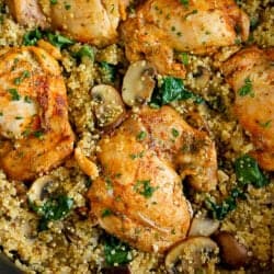 Chicken thighs, cooked quinoa, mushrooms and spinach in a black skillet.