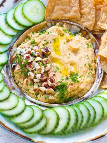 Roasted cauliflower dip with chopped pecans and parsley, surrounded by cucumber slices.