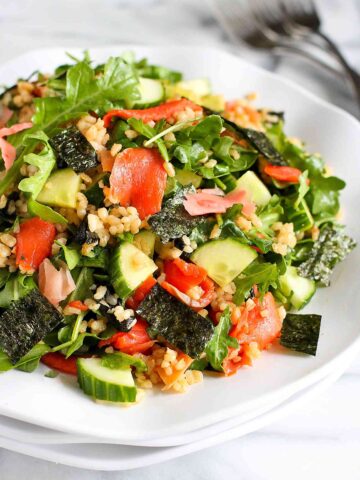 Salad with salmon, nori, cucumber, rice, ginger and arugula on a white plate.