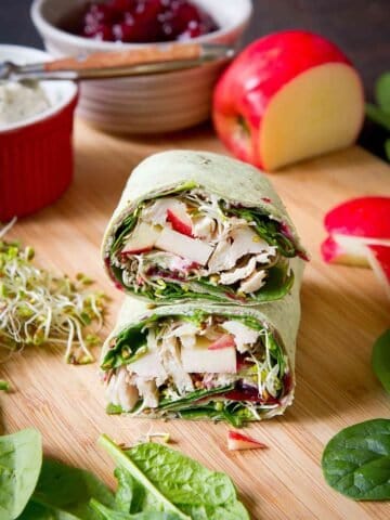 Turkey, cranberry and vegetable wrap sandwich. Apple, broccoli sprouts and bowls in the background.