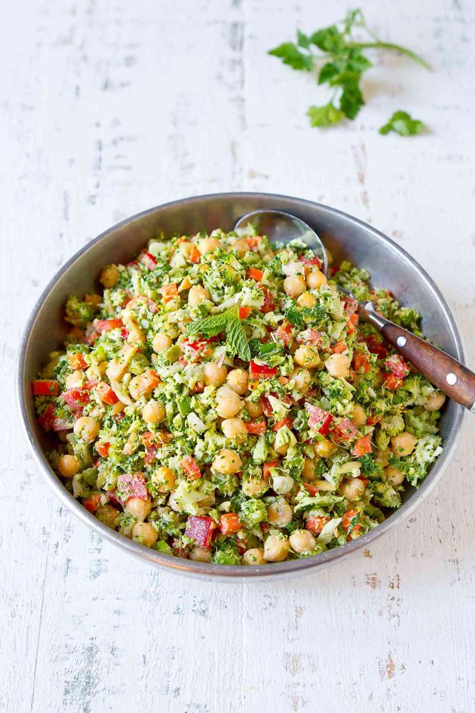 Chopped broccoli salad with red pepper, chickpeas and carrot in a silver bowl.