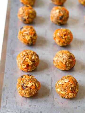 No-bake energy bites filled with shredded carrots and raisins, lined up on baking sheet.