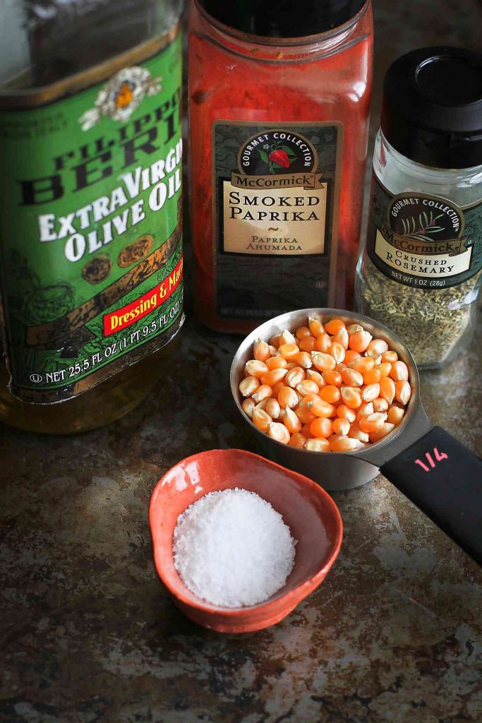 Popcorn kernels, olive oil, smoked paprika, rosemary and salt on a baking sheet.