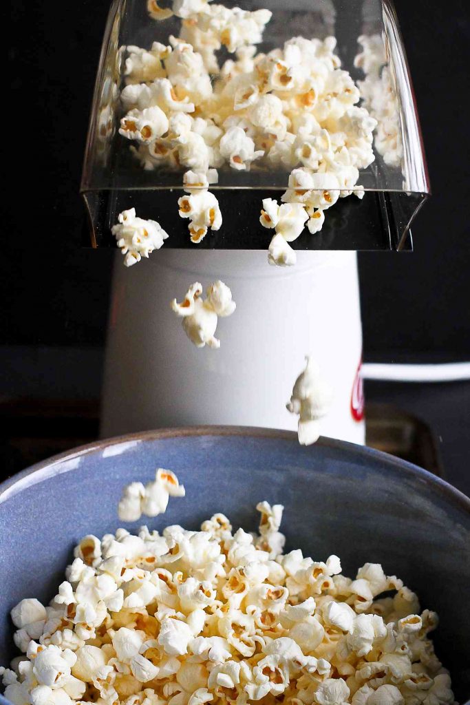 Popcorn coming out of an air popper and falling into a blue bowl