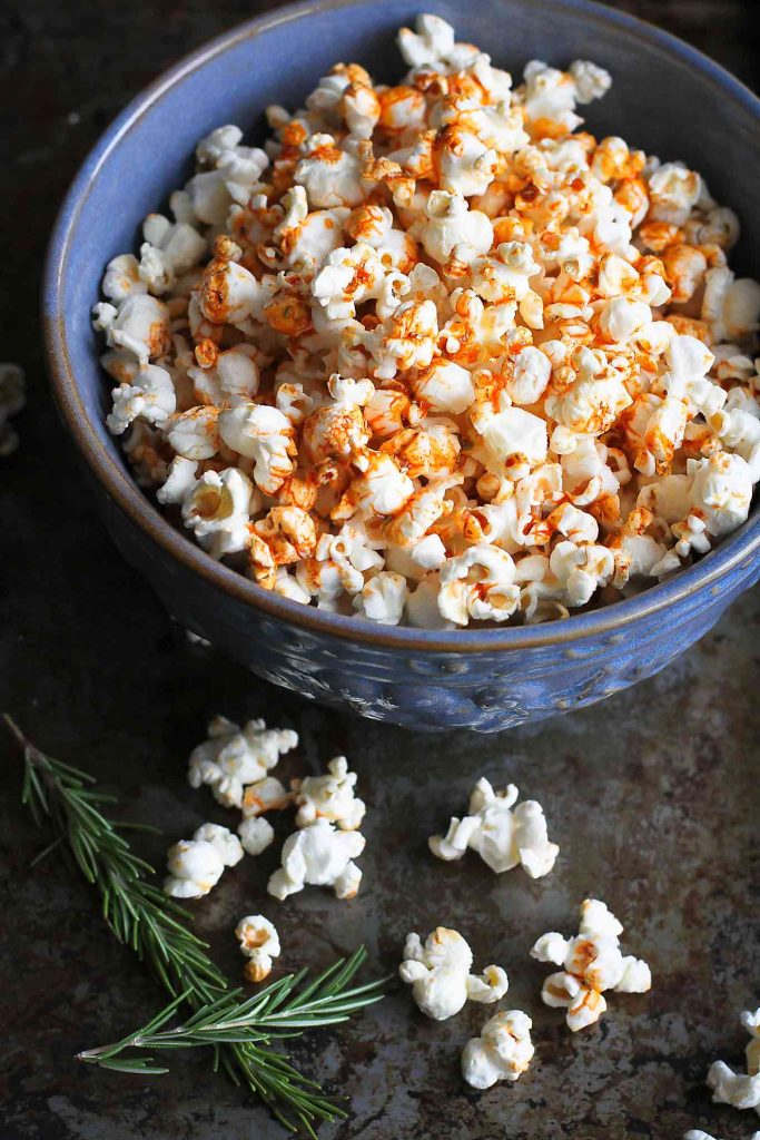 Popcorn in a large blue bowl. Topped with an olive oil, smoked paprika and rosemary mixture.