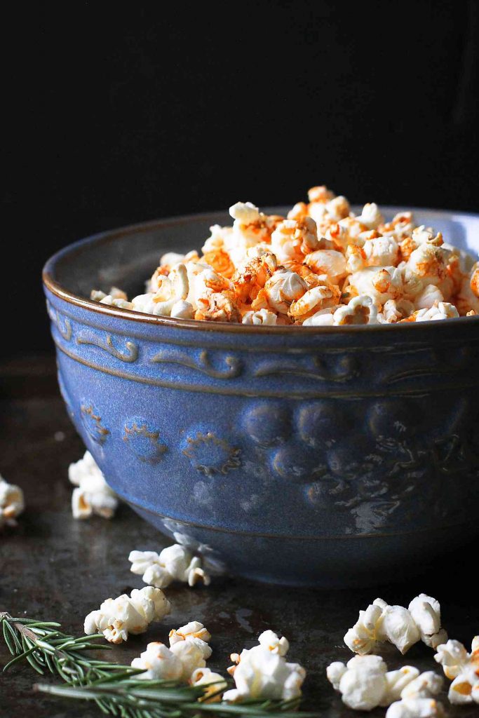 Popcorn topped with olive oil, smoked paprika and rosemary in a large blue bowl.