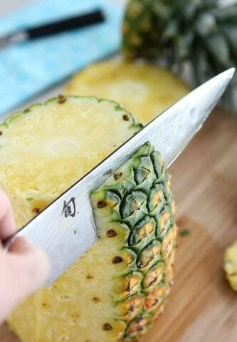 A large chef's knife slicing the skin from a pineapple.