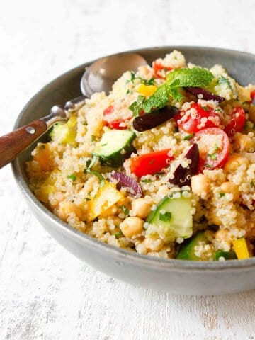 Quinoa salad with tomato, cucumber, bell pepper, herbs and olives in a gray bowl.