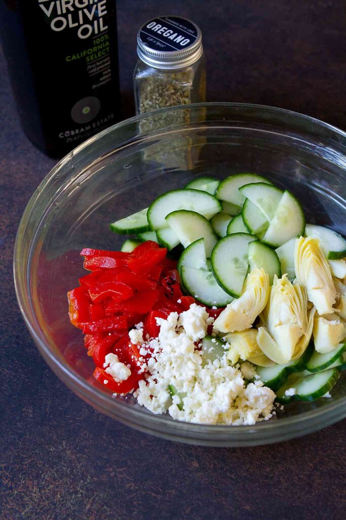 Sliced cucumber, roasted red pepper and artichoke hearts on a cutting board.