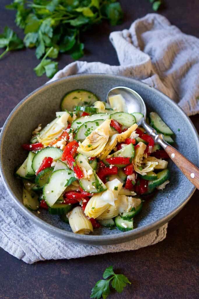 Salad with cucumber, roasted red pepper, artichokes and feta in a gray bowl.