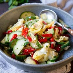 Mediterranean cucumber salad, with roasted peppers and artichokes in a gray bowl.