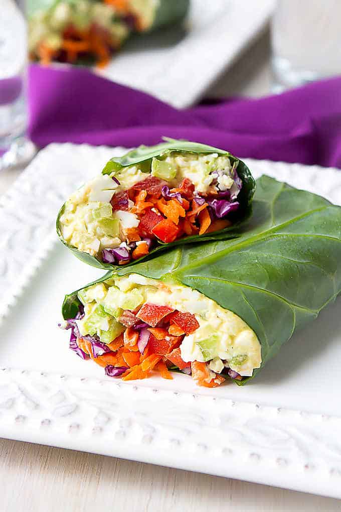 Collard green wraps filled with egg salad and vegetables, on a white plate.