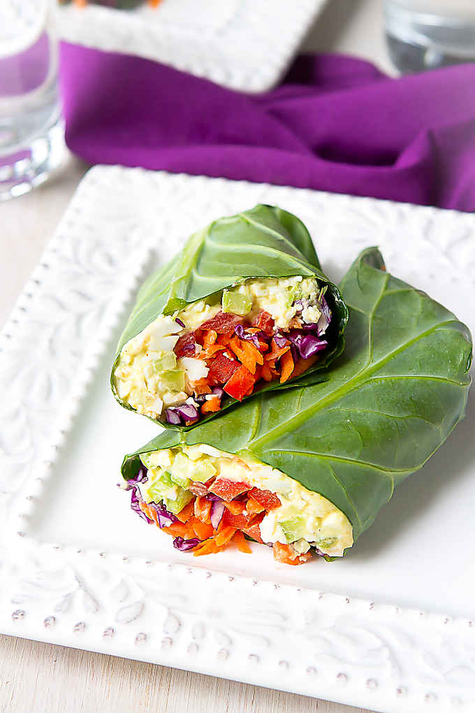 Egg salad collard green wraps with vegetables on a white plate.