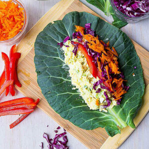 Collard green leaf topped with egg salad and vegetables, on a bamboo cutting board.