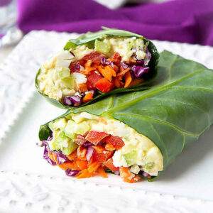 Egg salad collard green wraps with vegetables on a white plate.