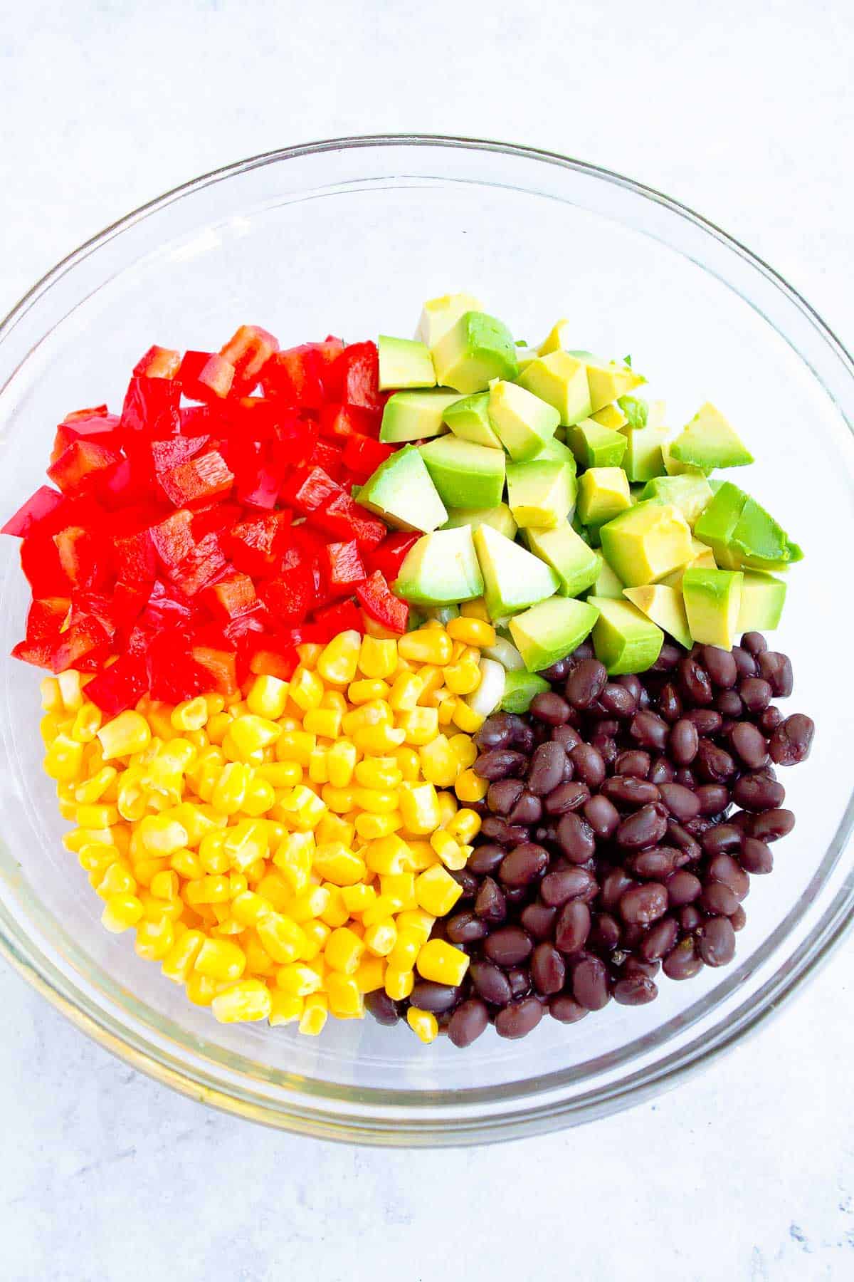 Black beans, corn, avocado and red bell pepper in a glass bowl.