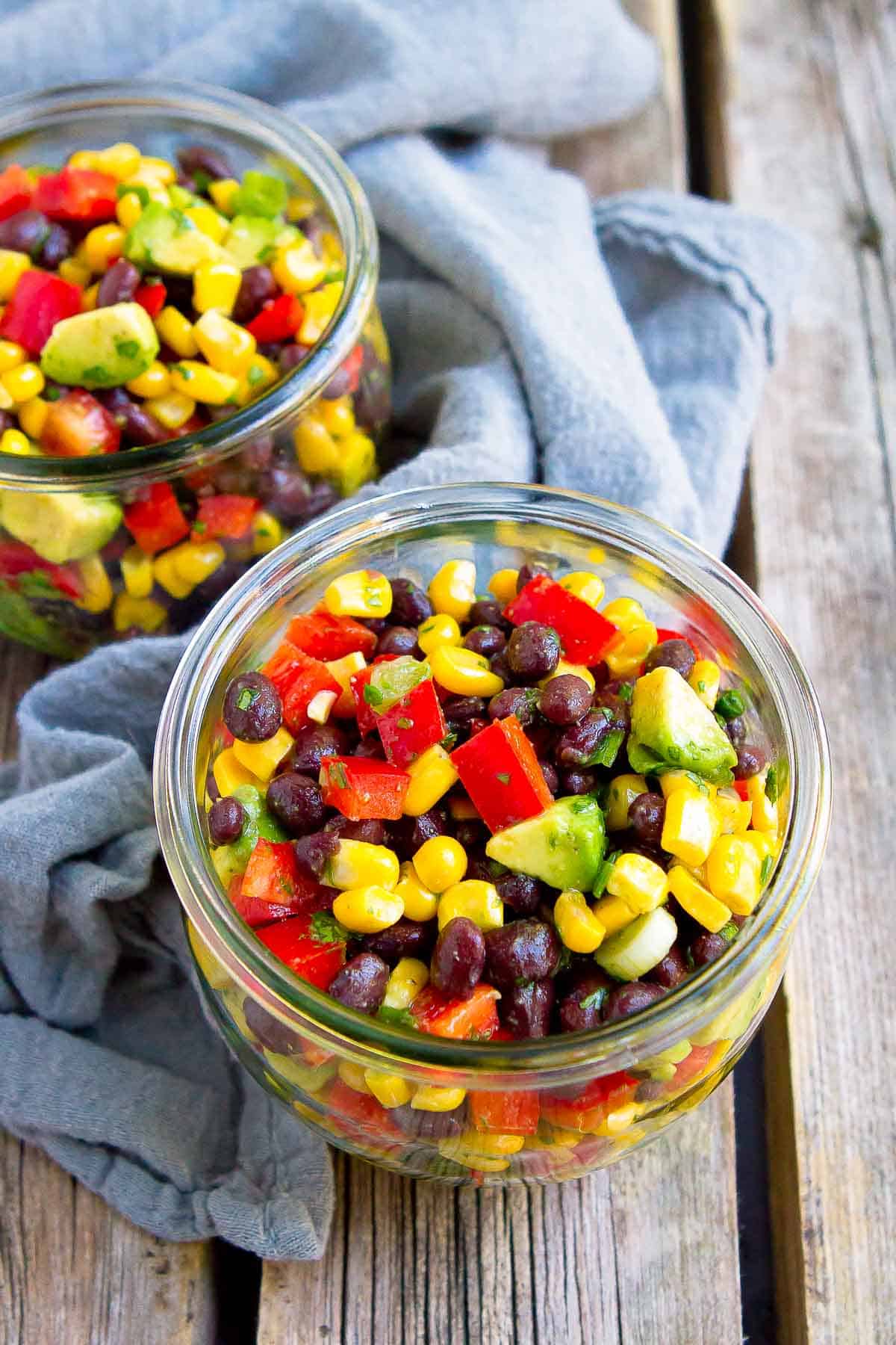 Corn, beans, peppers and avocado in canning jars, with gray napkin.