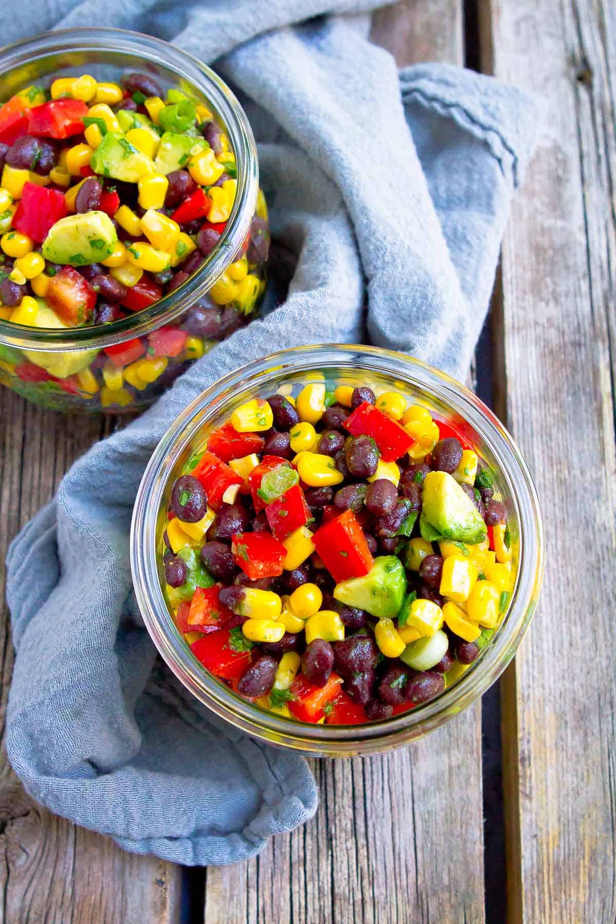 Overhead photo of corn bean salad in glass jars on wooden table.