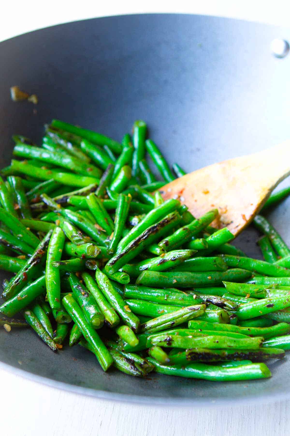 Green beans in a nonstick wok with a wooden spoon.