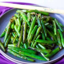 Stir fried green beans and chopsticks on a gray plate, sitting on a purple napkin.