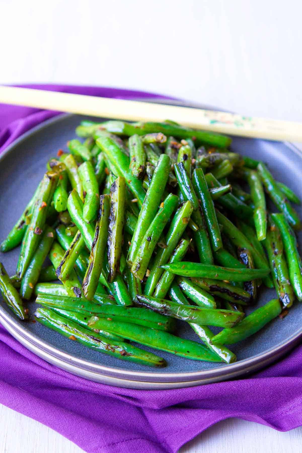 Stir fried green beans and chopsticks on a gray plate, sitting on a purple napkin.