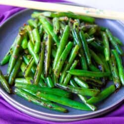 Stir fried green beans and chopsticks on a gray plate, sitting on a purple napkin.