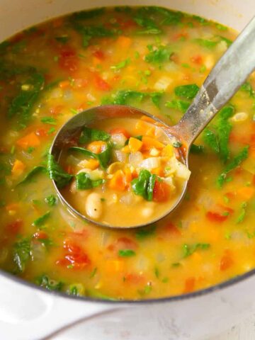 White bean soup in a large white saucepan with silver ladle.