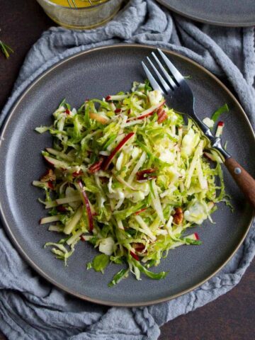 Apple and shredded Brussels sprouts slaw on gray plates, with gray napkin.